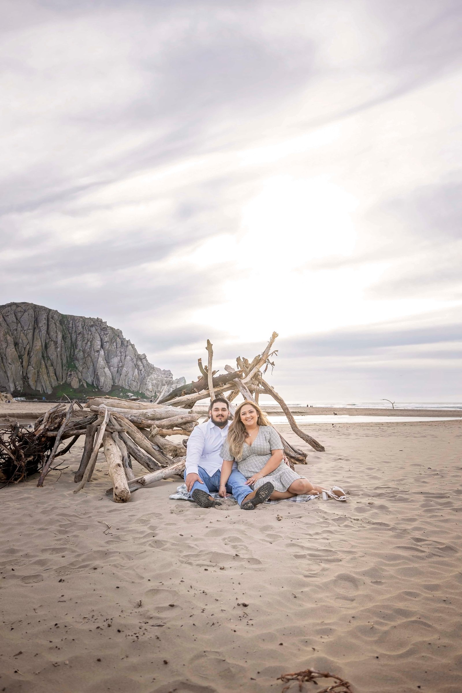 couple sitting in the sand by some driftwood at the beach