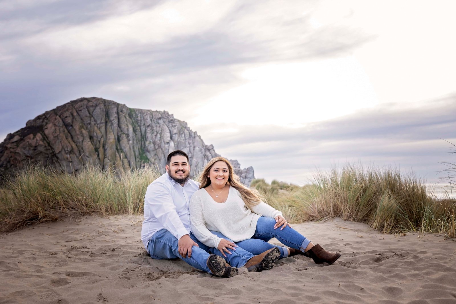 couple sitting in the sand with Morro Rock behind them